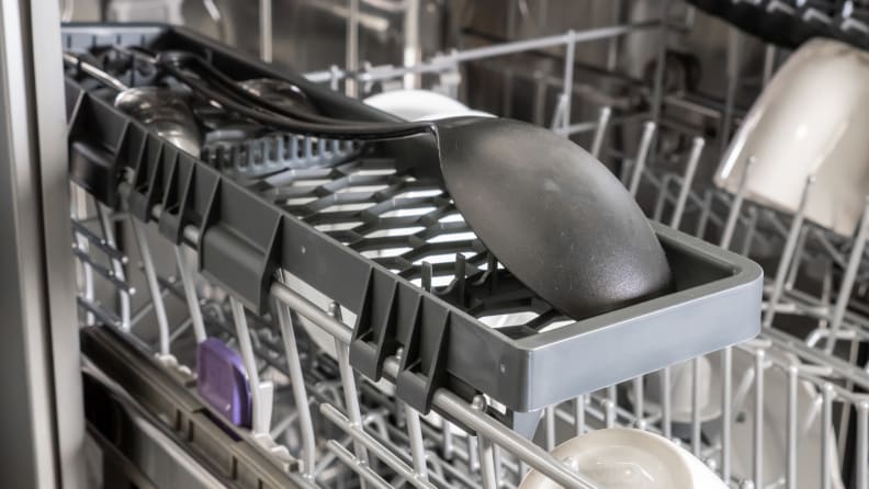 A spatula lays upside down on the side rack of a dishwasher
